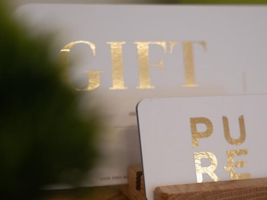 A Pure Aesthetics Clinic gift card in gold lettering on a wooden stand